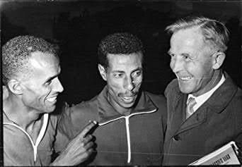 Abebe Bikila, centre, smiling between another athlete and Onni Niskanen.