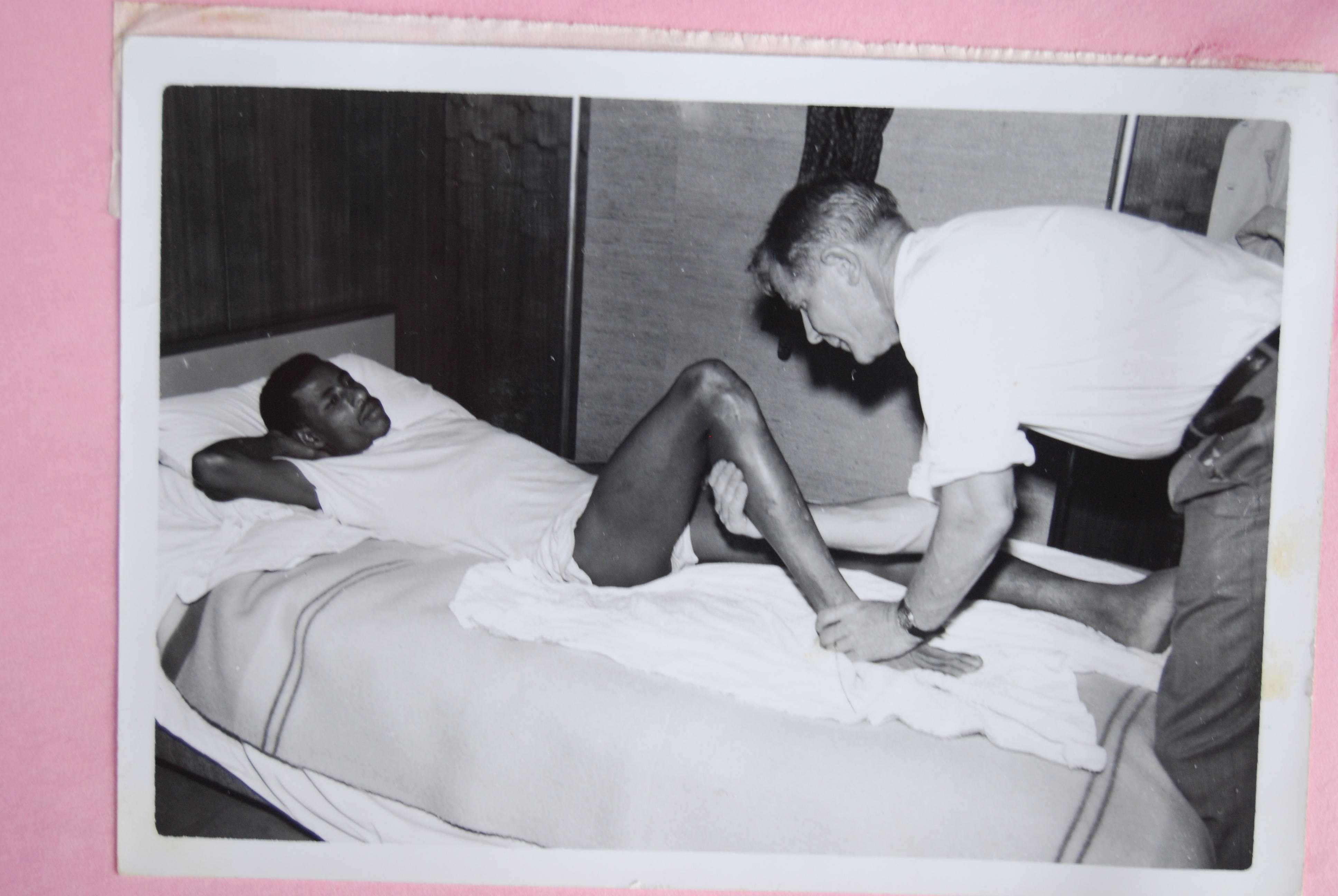 Onni Niskanen leaning over Abebe Bikila, who lies on a bed while Niskanen works on his leg.